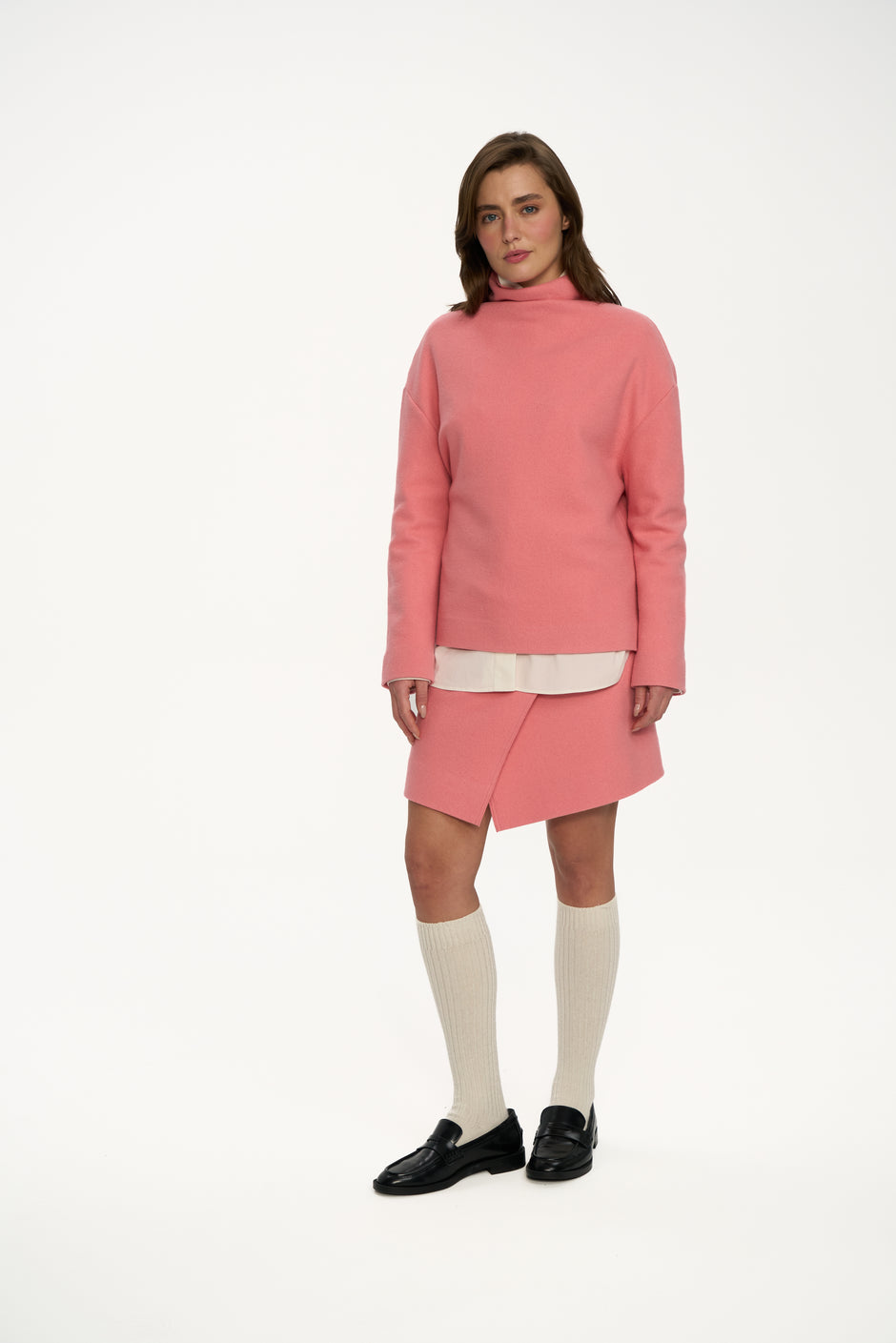 Powder pink pure wool high-neck sweater styled with matching wrap mini skirt, cream shirt hem, knee-high socks and black loafers on model, full length front view – Inner Tiger