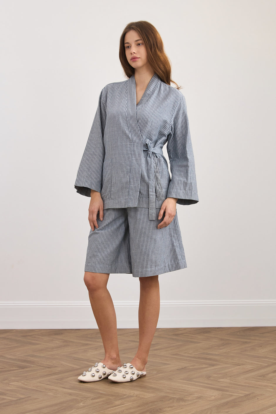 Woman wearing a blue striped robe and shorts set on a plain background