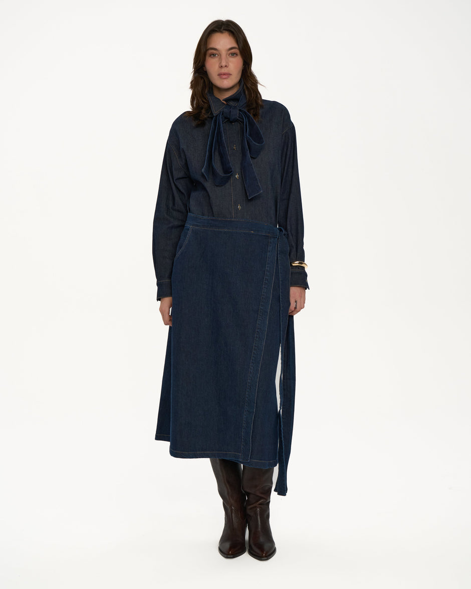 Woman wearing a dark blue denim 
outfit with a long skirt on a white background