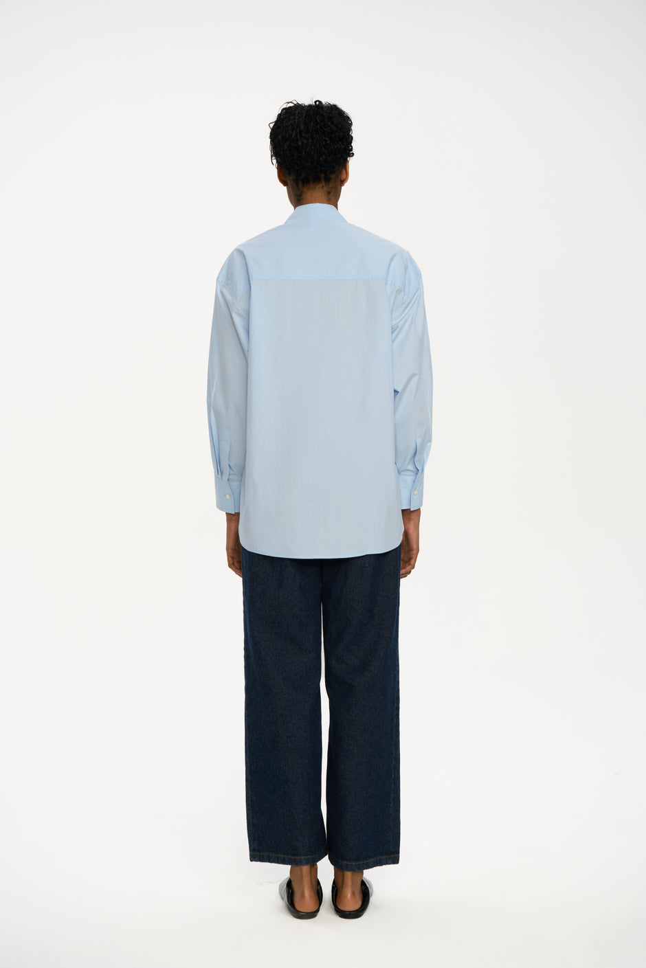 Light blue cotton breastfeeding-friendly shirt with flap detail styled with dark indigo wide-leg jeans and black pointed shoes, full length back view – Inner Tiger