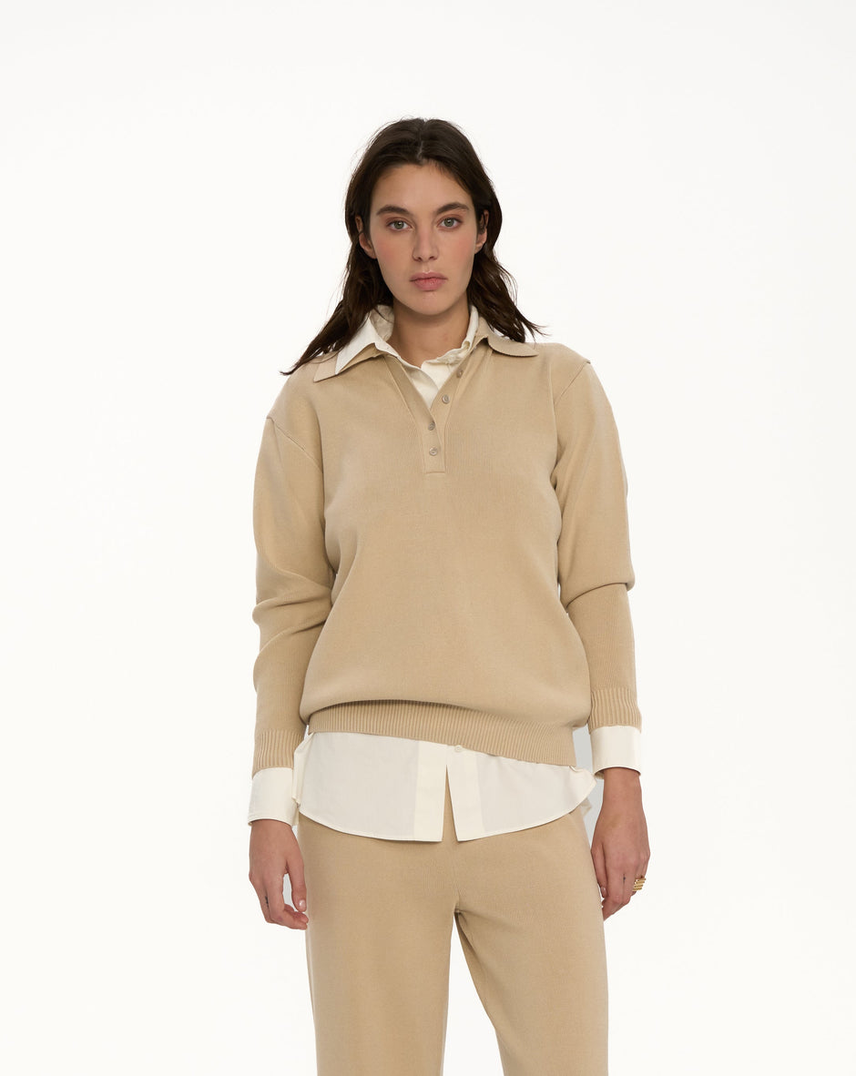 Woman wearing a beige outfit with a white shirt underneath on a white background