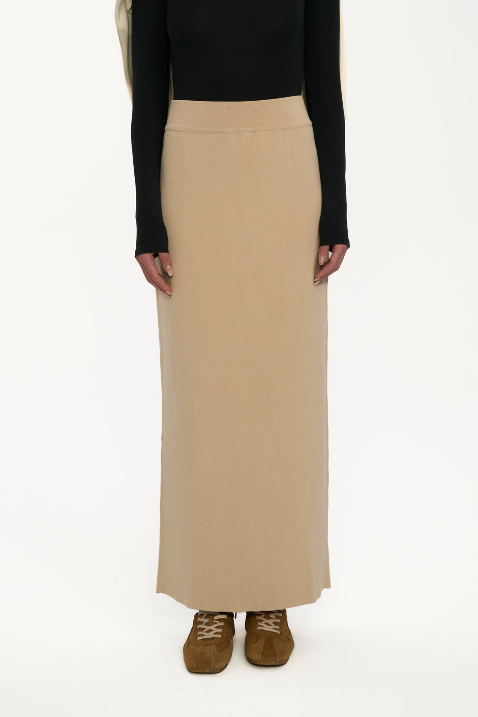 Person wearing a black top and beige skirt on a white background