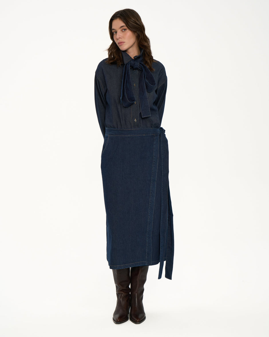 Model wearing a dark blue denim matching set with a skirt and blouse on a white background