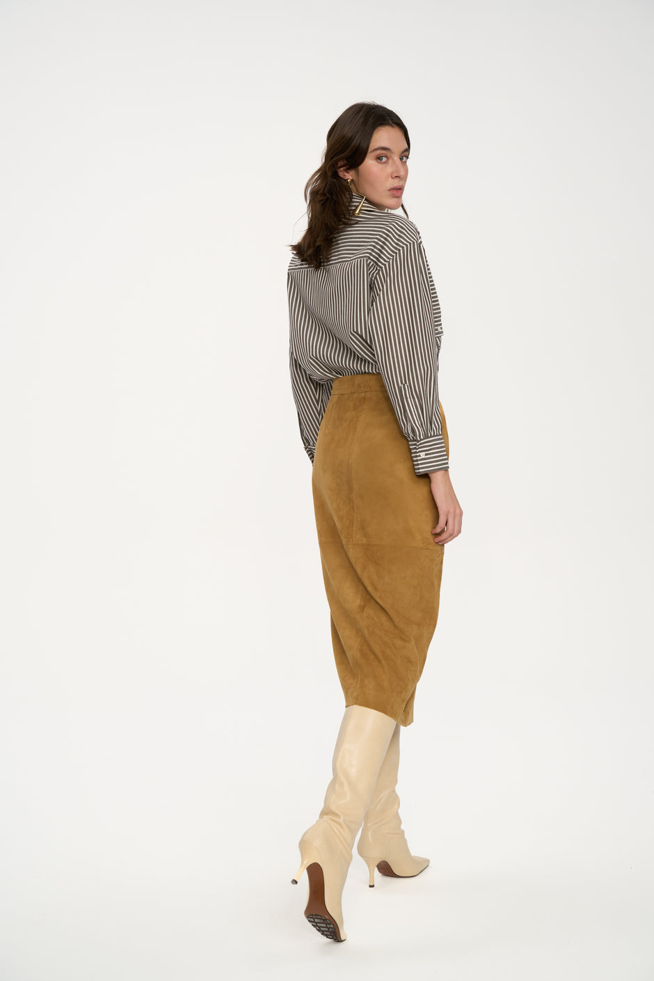 Woman wearing a striped shirt, brown skirt, and beige boots on a white background