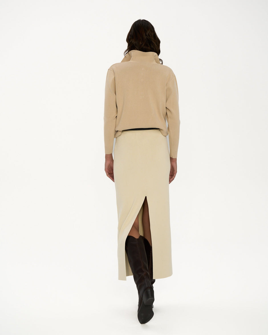 Person wearing a beige coat and skirt with black boots on a white background